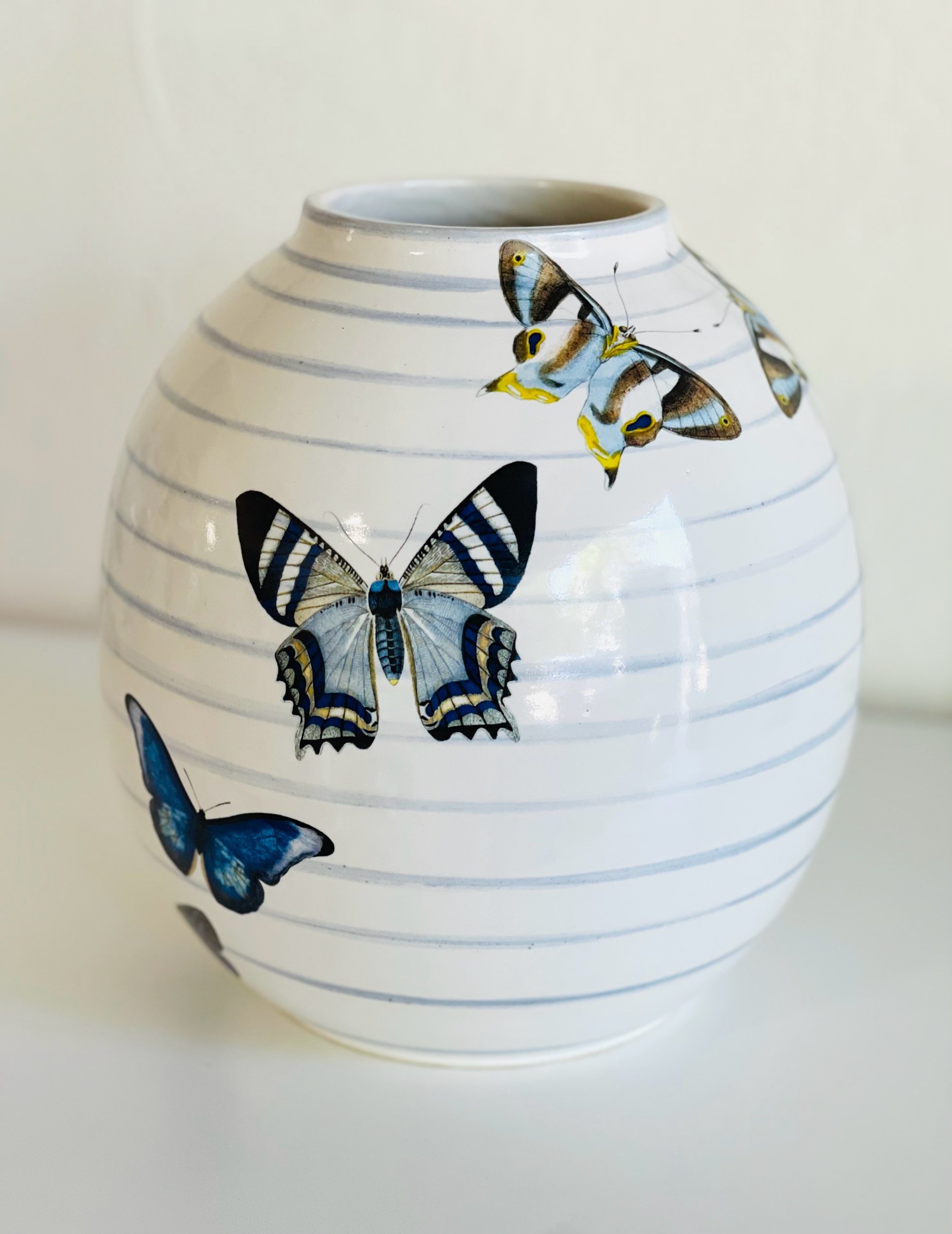 Large white stoneware orb vase with light blue bands and colorful butterfly decals