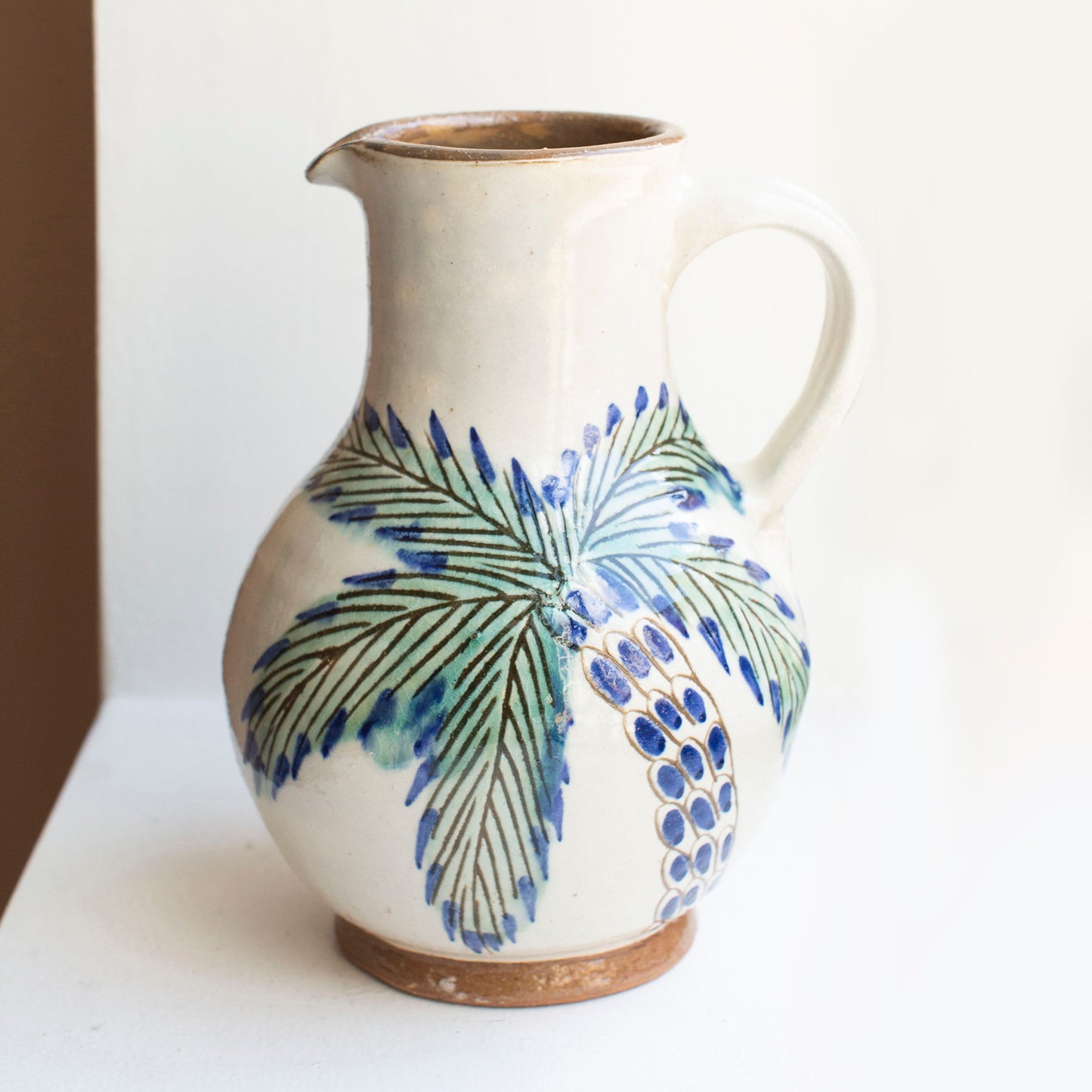 Handmade ceramic pitcher with a lively palm depiction in natural glazed clay